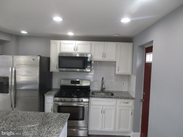 kitchen featuring stone countertops, white cabinetry, stainless steel appliances, and a sink