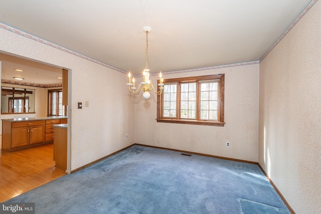 empty room with crown molding, light colored carpet, baseboards, wallpapered walls, and a notable chandelier