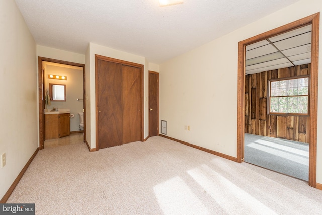 unfurnished bedroom with a closet, wood walls, ensuite bathroom, and light carpet