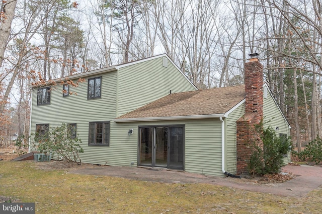 back of property with a shingled roof and a chimney