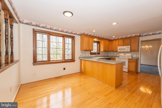 kitchen with white appliances, a notable chandelier, light wood-style flooring, and a peninsula