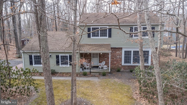 view of front of home featuring covered porch, brick siding, and roof with shingles