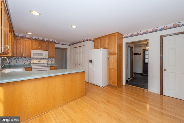 kitchen featuring a peninsula, white appliances, tasteful backsplash, a sink, and light wood-type flooring