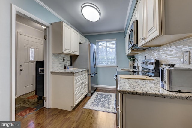 kitchen featuring crown molding, dark wood-type flooring, light stone counters, stainless steel appliances, and white cabinetry