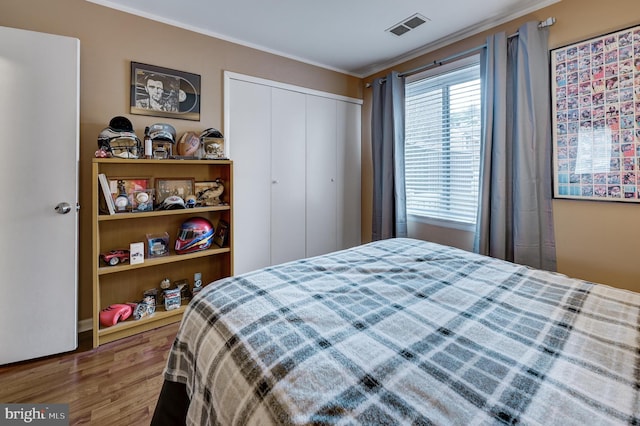 bedroom featuring wood finished floors, visible vents, a closet, and ornamental molding