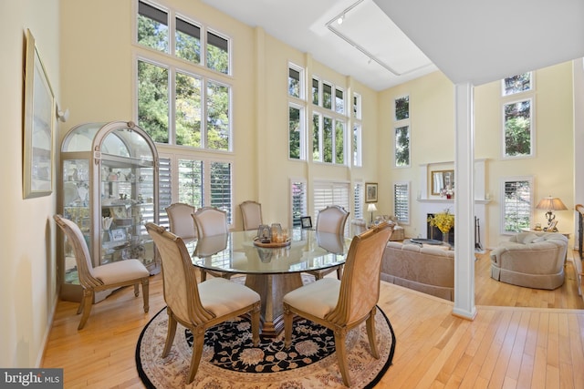 dining room featuring a fireplace, light wood-style flooring, and a towering ceiling