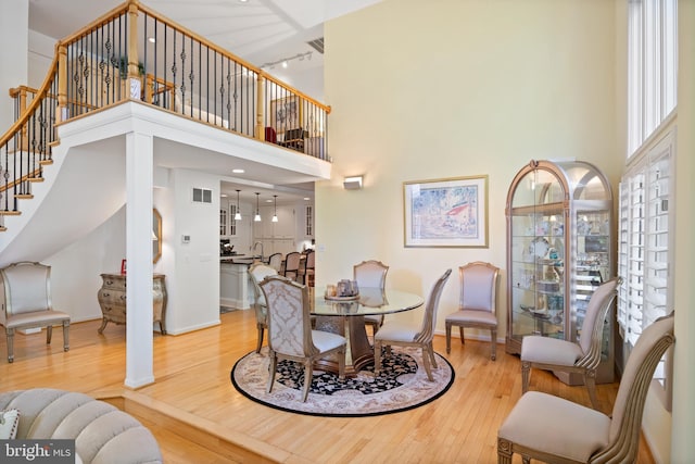 dining room with a towering ceiling, light wood-style floors, and stairs