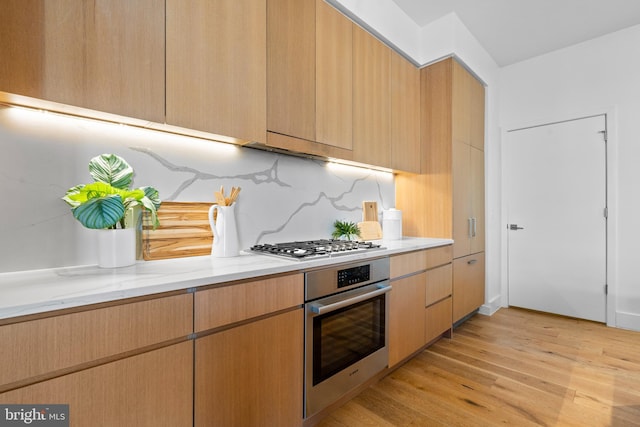 kitchen with light wood-type flooring, light brown cabinetry, stainless steel appliances, decorative backsplash, and light stone countertops