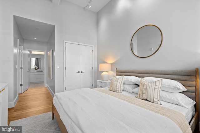 bedroom featuring light wood finished floors, track lighting, baseboards, a towering ceiling, and a closet