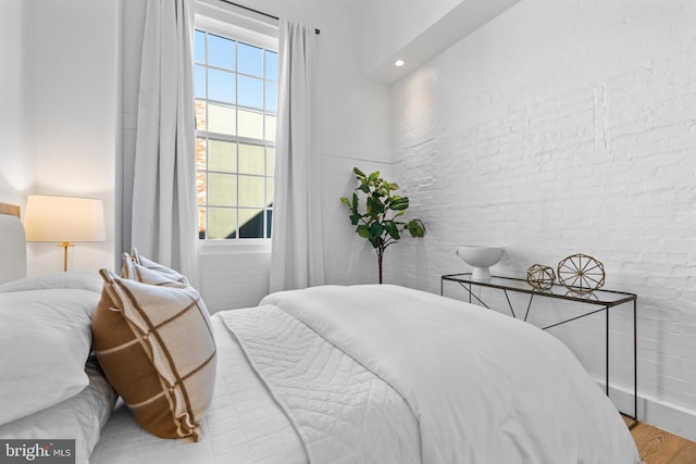 bedroom with wood finished floors and brick wall