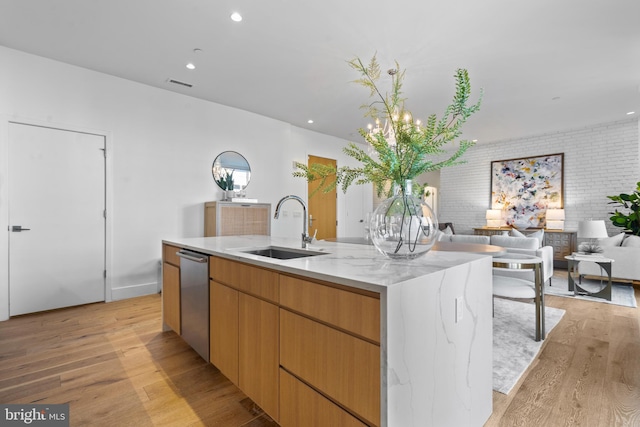 kitchen with visible vents, open floor plan, a center island with sink, light wood-style flooring, and a sink