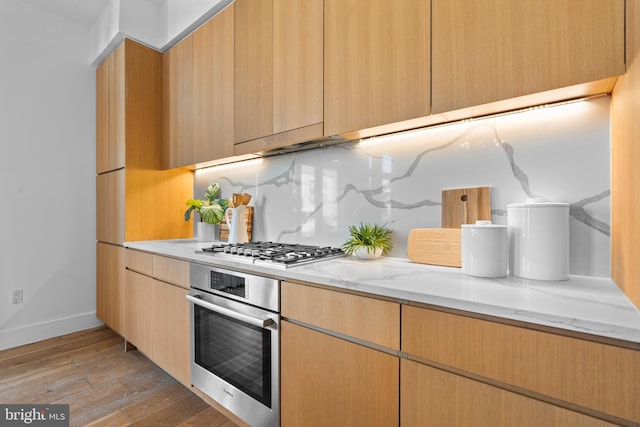 kitchen with light stone counters, baseboards, light wood-style flooring, appliances with stainless steel finishes, and backsplash