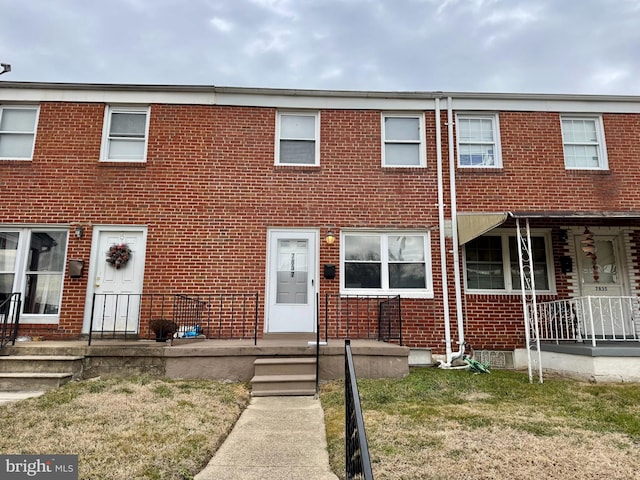 view of property with covered porch, brick siding, and a front lawn