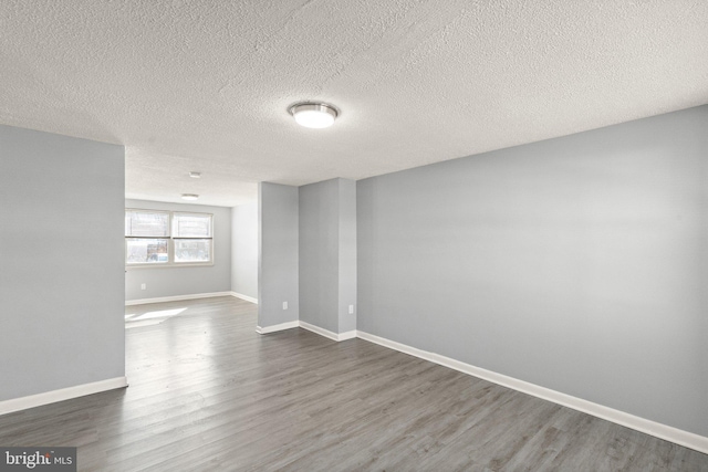 empty room featuring a textured ceiling, dark wood finished floors, and baseboards