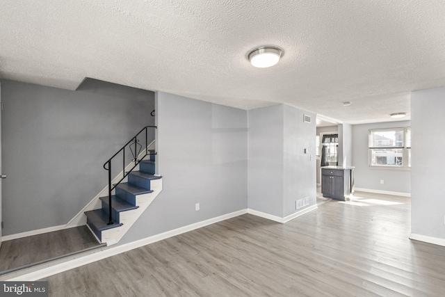 interior space featuring a textured ceiling, wood finished floors, visible vents, baseboards, and stairway