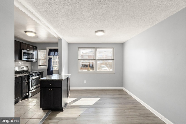 kitchen with baseboards, appliances with stainless steel finishes, light stone countertops, light wood-type flooring, and backsplash