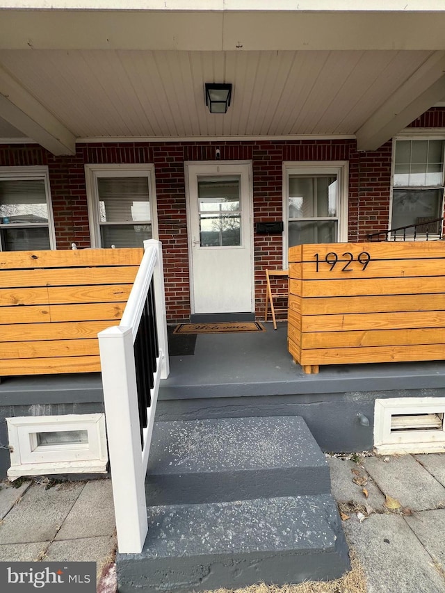 doorway to property with a porch and brick siding