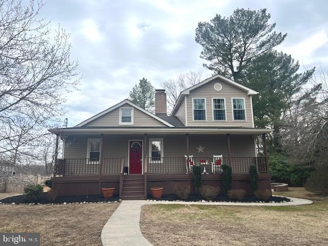 view of front facade with covered porch, a chimney, and a front lawn