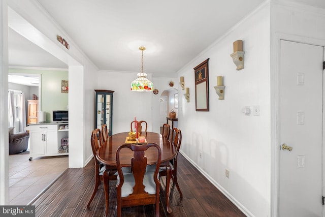 dining area with ornamental molding, arched walkways, dark wood-style flooring, and baseboards