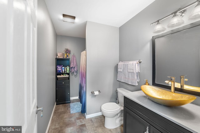 bathroom featuring toilet, stone finish floor, baseboards, and vanity