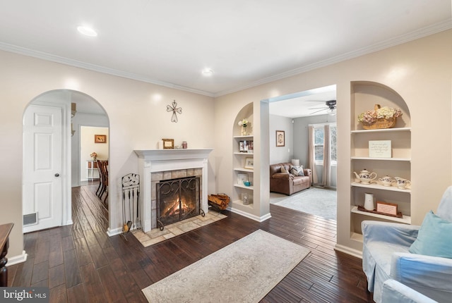 living area with built in shelves, a tile fireplace, visible vents, dark wood-style floors, and crown molding