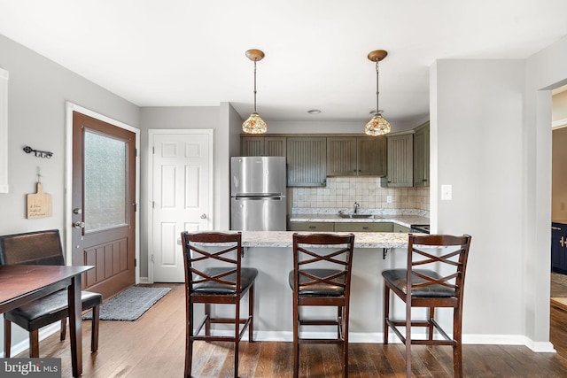 kitchen with a breakfast bar, decorative light fixtures, decorative backsplash, light wood-style floors, and freestanding refrigerator