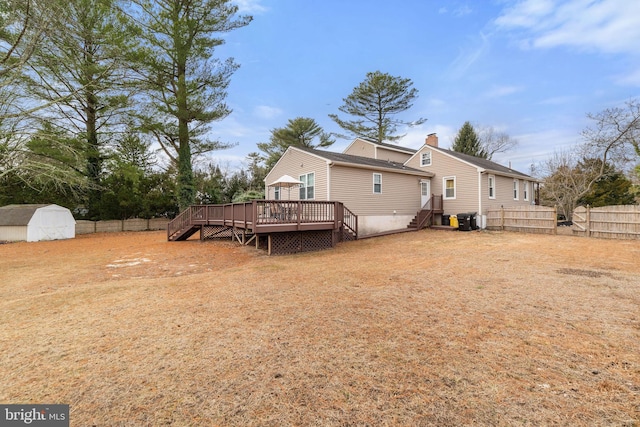 back of property featuring a deck, a storage unit, a chimney, and fence