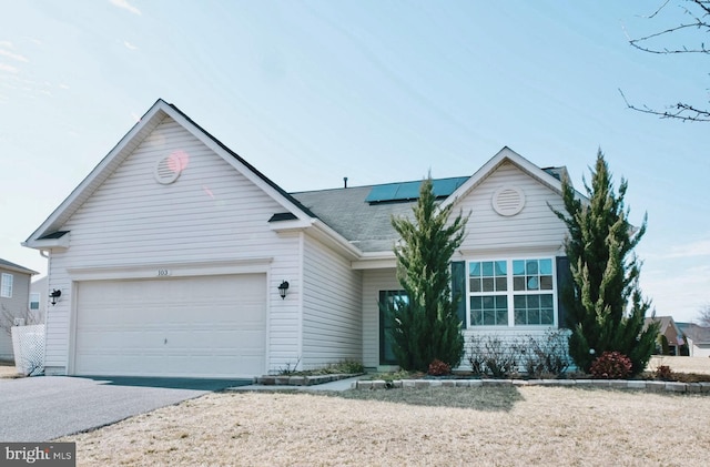 ranch-style house featuring a garage, aphalt driveway, and solar panels