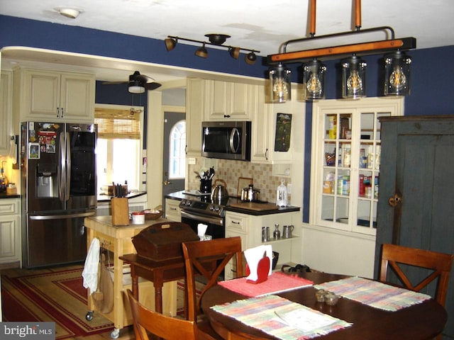 kitchen with appliances with stainless steel finishes, dark countertops, glass insert cabinets, and tasteful backsplash