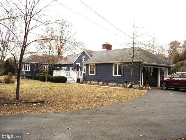 ranch-style house with covered porch, roof with shingles, driveway, and a chimney