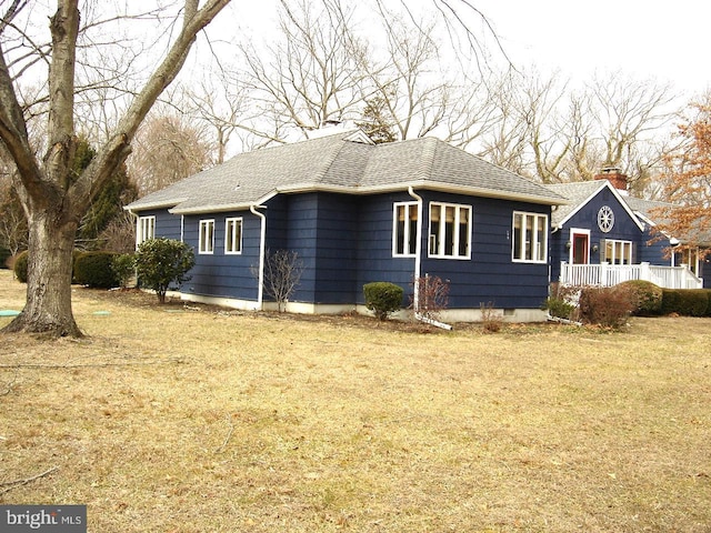 view of side of home featuring roof with shingles and a yard