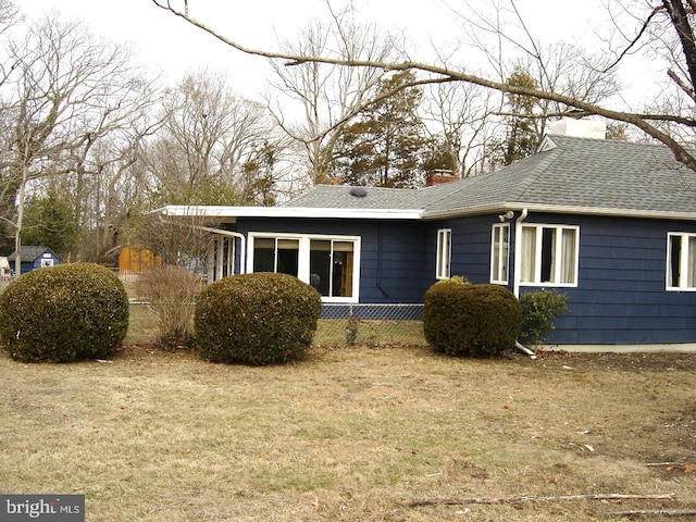 back of house with a shingled roof, a chimney, fence, and a lawn