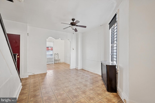 interior space with light tile patterned floors, baseboards, arched walkways, and a ceiling fan