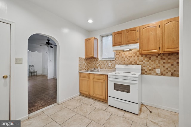 kitchen with arched walkways, under cabinet range hood, white range oven, light countertops, and backsplash