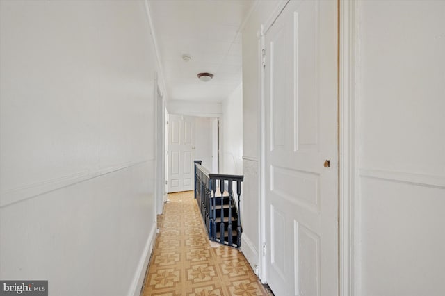 hall featuring light floors, baseboards, and an upstairs landing