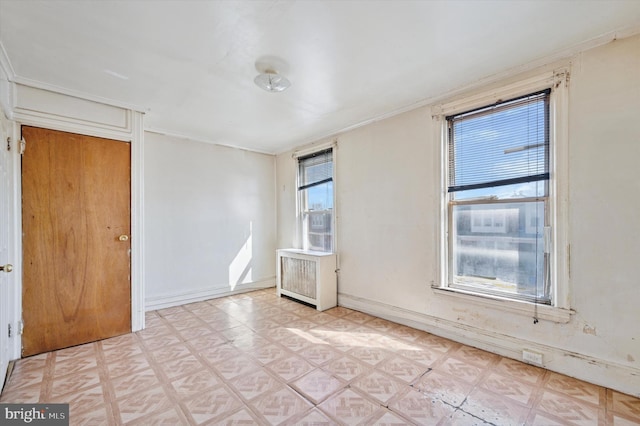 spare room with light floors, ornamental molding, radiator, and baseboards