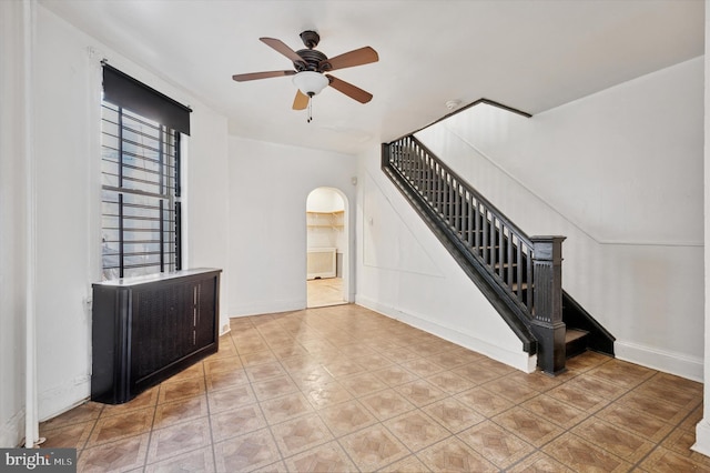 interior space with baseboards, stairs, arched walkways, and a ceiling fan