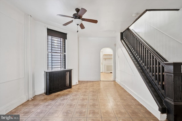 interior space with light tile patterned floors, baseboards, arched walkways, a ceiling fan, and stairs