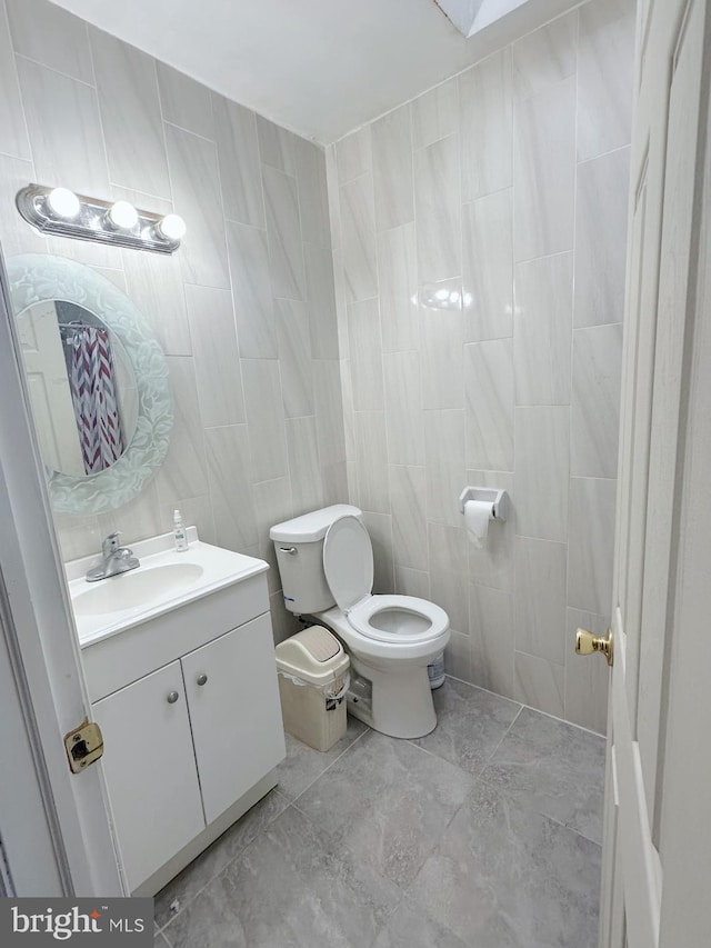 half bathroom with toilet, tile walls, and vanity