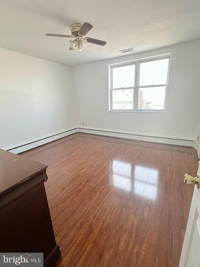 empty room featuring a ceiling fan, visible vents, a baseboard heating unit, and wood finished floors