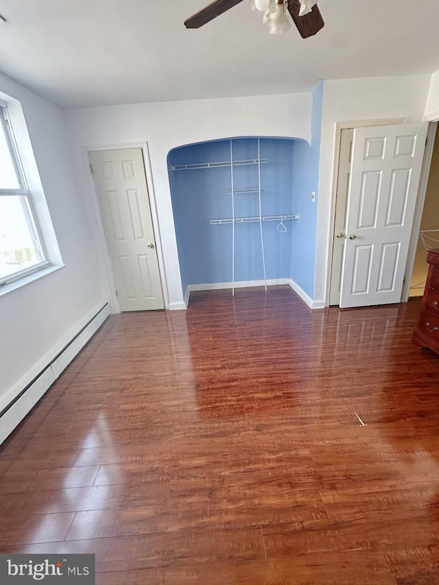 unfurnished bedroom featuring arched walkways, ceiling fan, a baseboard radiator, wood finished floors, and baseboards