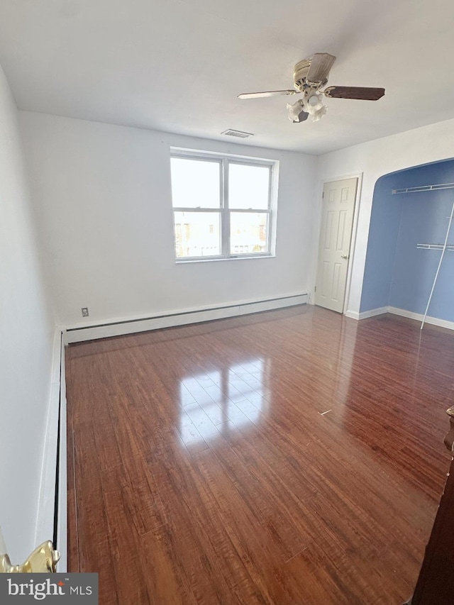 unfurnished bedroom featuring ceiling fan, a baseboard radiator, wood finished floors, visible vents, and baseboards