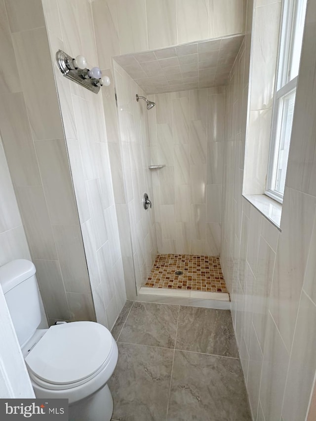 bathroom with tiled shower, tile walls, toilet, and tile patterned floors