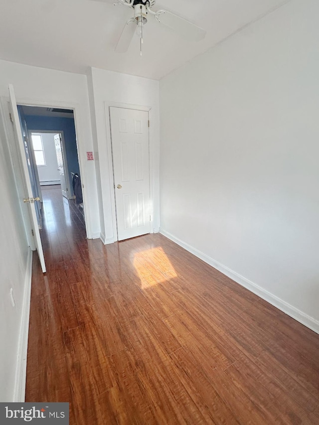 spare room featuring a ceiling fan, baseboard heating, baseboards, and wood finished floors