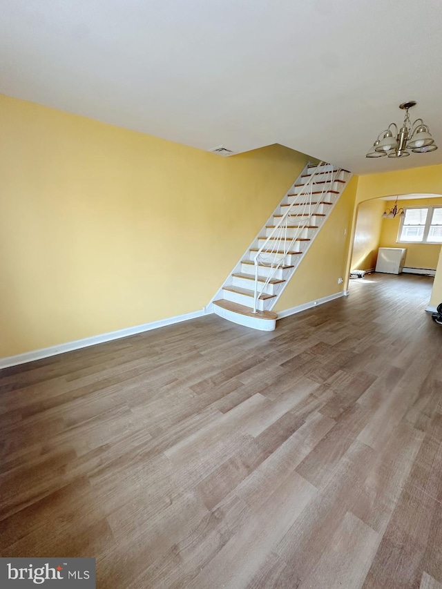 spare room featuring baseboards, visible vents, stairway, wood finished floors, and a chandelier