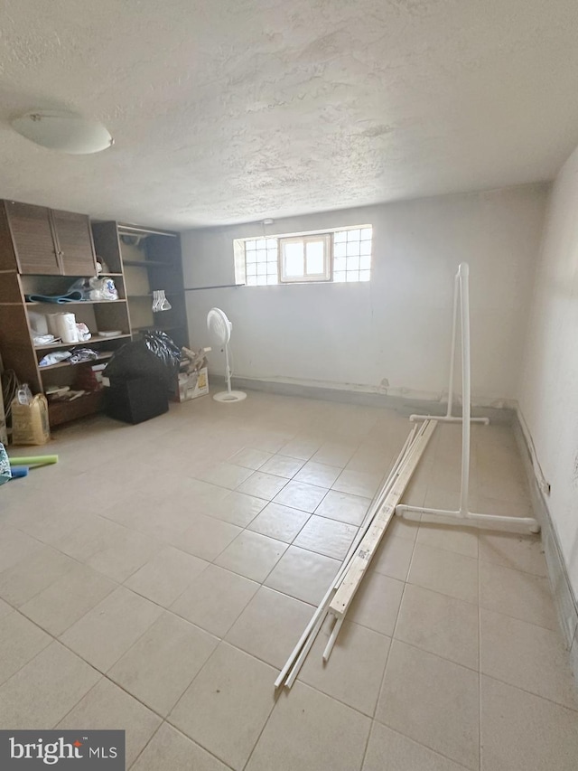 below grade area featuring a textured ceiling, baseboards, and light tile patterned floors