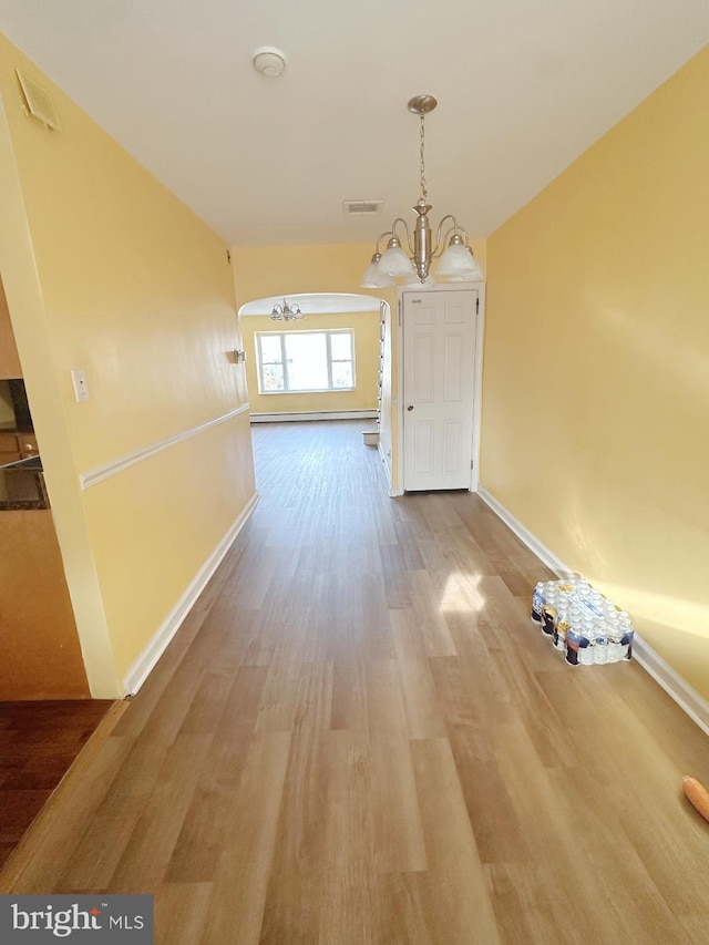 hallway with an inviting chandelier, wood finished floors, visible vents, and baseboards