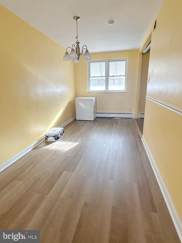 unfurnished dining area with a notable chandelier, a baseboard heating unit, wood finished floors, and baseboards