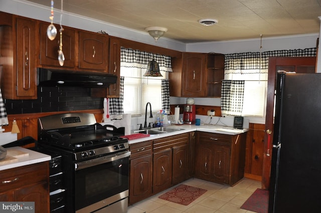 kitchen featuring under cabinet range hood, a sink, light countertops, freestanding refrigerator, and stainless steel range with gas stovetop