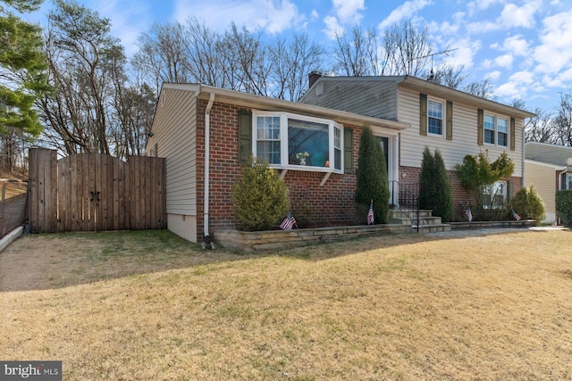 tri-level home featuring fence, a front lawn, and brick siding